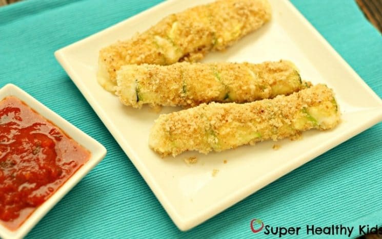 bread crumb coated zucchini sticks on a white plate served with marinara sauce
